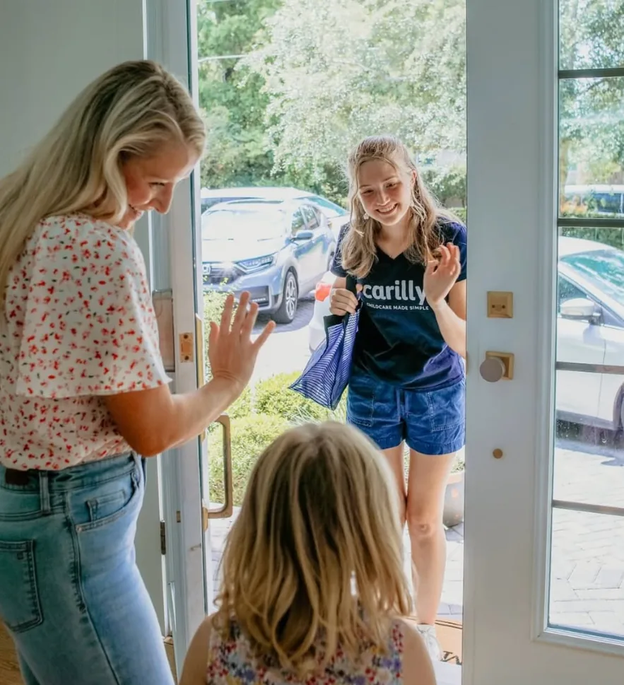A Carilly nanny in a Carilly shirt greeting a mother and daughter at their front door