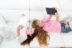 kid girls having fun playing with tablet pc lying sofa